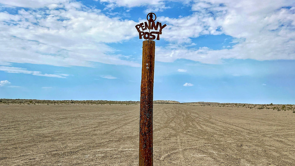 Weathered post in barren desert, displaying "Penny Post" sign against a blue sky with clouds. Desolate and rustic atmosphere.