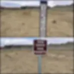 Desert landscape with two signs: "No Motor Vehicles" allowing foot and bike travel, and "Cross Country Travel Prohibited". Rocky hills in the backdrop.