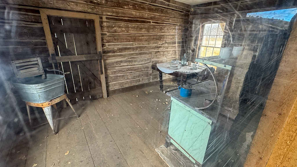 Interior of a rustic wooden cabin with aged furniture. A blue pot and wash bin are visible. Light filters through a window, adding warmth.