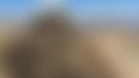 Pile of rocks atop a mountain with vast desert landscape in the background. Bright, sunny day with scattered clouds in a blue sky.