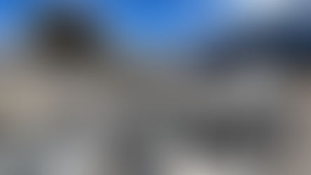 Rocky terrain with large boulders in the foreground. Snow-capped mountains and blue sky fill the background, creating a serene landscape.