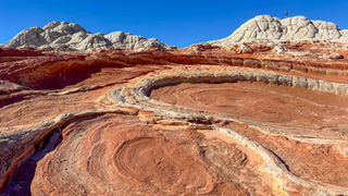 White and red rock formations under clear blue sky, with swirling patterns in the desert landscape. No visible text or people.