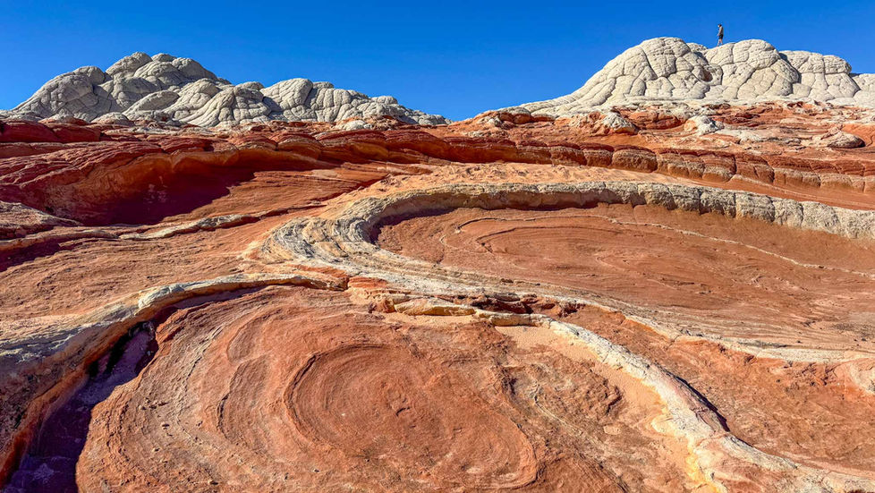 White and red rock formations under clear blue sky, with swirling patterns in the desert landscape. No visible text or people.