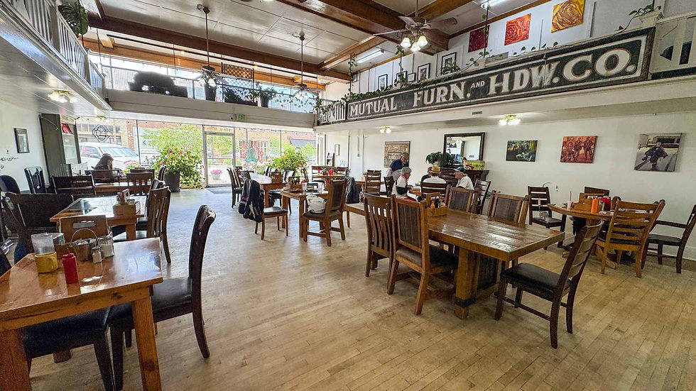 Bright vintage restaurant with wooden tables, a few diners, and a large MUTUAL FURN. AND HDW. CO. sign above the mezzanine.