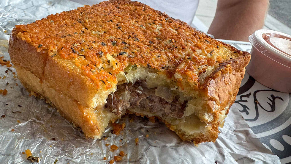 Half-eaten cheesy garlic bread sandwich on foil, golden crust with herbs and melted filling, beside a small dipping sauce cup.