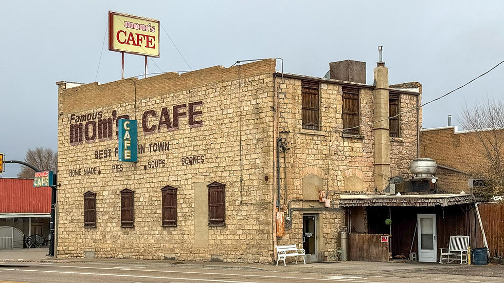 Stone building of Mom's Cafe with signs reading "Famous Mom's Cafe" and "Best in Town." Rustic setting with muted colors and closed windows.