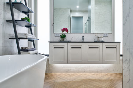 Modern bathroom with freestanding bathtub and double vanity. Modern bathroom featuring a freestanding bathtub, floating vanity and marble finishes. Contemporary bathroom with floating double vanity, marble walls, freestanding bath and timber herringbone floor. Light-filled luxury bathroom with freestanding tub, custom vanity, marble surfaces and soft under-cabinet lighting. Designer bathroom showcasing a floating vanity, freestanding bath, marble tiles and warm timber flooring.
