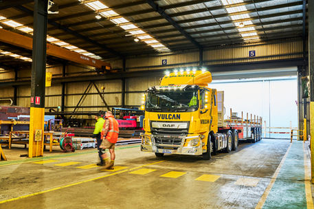 DAF truck with a flatbed trailer inside an industrial warehouse. A DAF truck branded Vulcan Steel, coupled with a Midland flatbed trailer inside a steel fabrication facility. Vulcan Steel transport operation featuring a DAF truck and Midland flatbed trailer inside an industrial warehouse. A Vulcan Steel DAF truck with a Midland flatbed trailer operating inside a steel fabrication warehouse, highlighting logistics, safety, and heavy transport capability. Steel transport operations using a DAF truck and Midland trailer within a Vulcan Steel facility