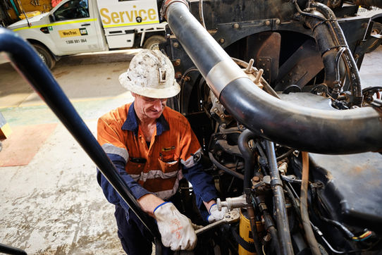 WesTrac technician servicing a Caterpillar machine engine in a workshop. A WesTrac technician wearing safety gear while servicing a Caterpillar machine engine inside a workshop. A WesTrac technician carrying out maintenance on a Caterpillar machine, highlighting hands-on service expertise and safety practices. A WesTrac service technician working on a Caterpillar machine engine in a workshop environment, demonstrating skilled maintenance and technical support. Caterpillar equipment maintenance in progress by a WesTrac technician during scheduled servicing.