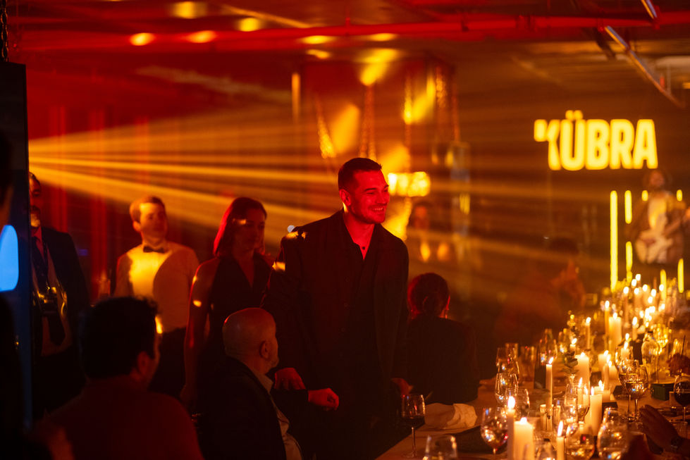 Netflix Kübra etkinlik gecesinin loş ve kırmızı ışıklı atmosferinde kalabalık arasında yer alan Çağatay Ulusoy profesyonel etkinlik fotoğrafı.