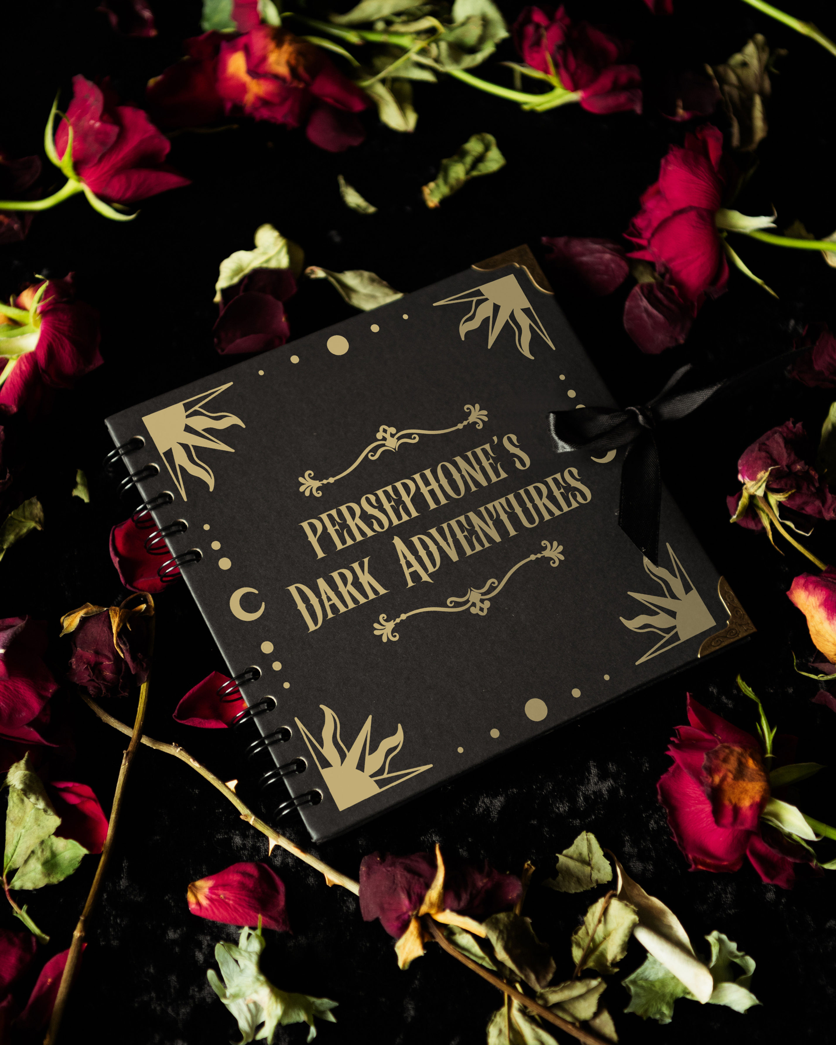 A black scrapbook with gold gothic text and a celestial inspired border that says "Persephone's Dark Adventures"