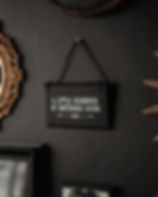 Black gothic wall sign with white lettering reading "A Little Reminder of Impending Doom," hanging on a dark wall.