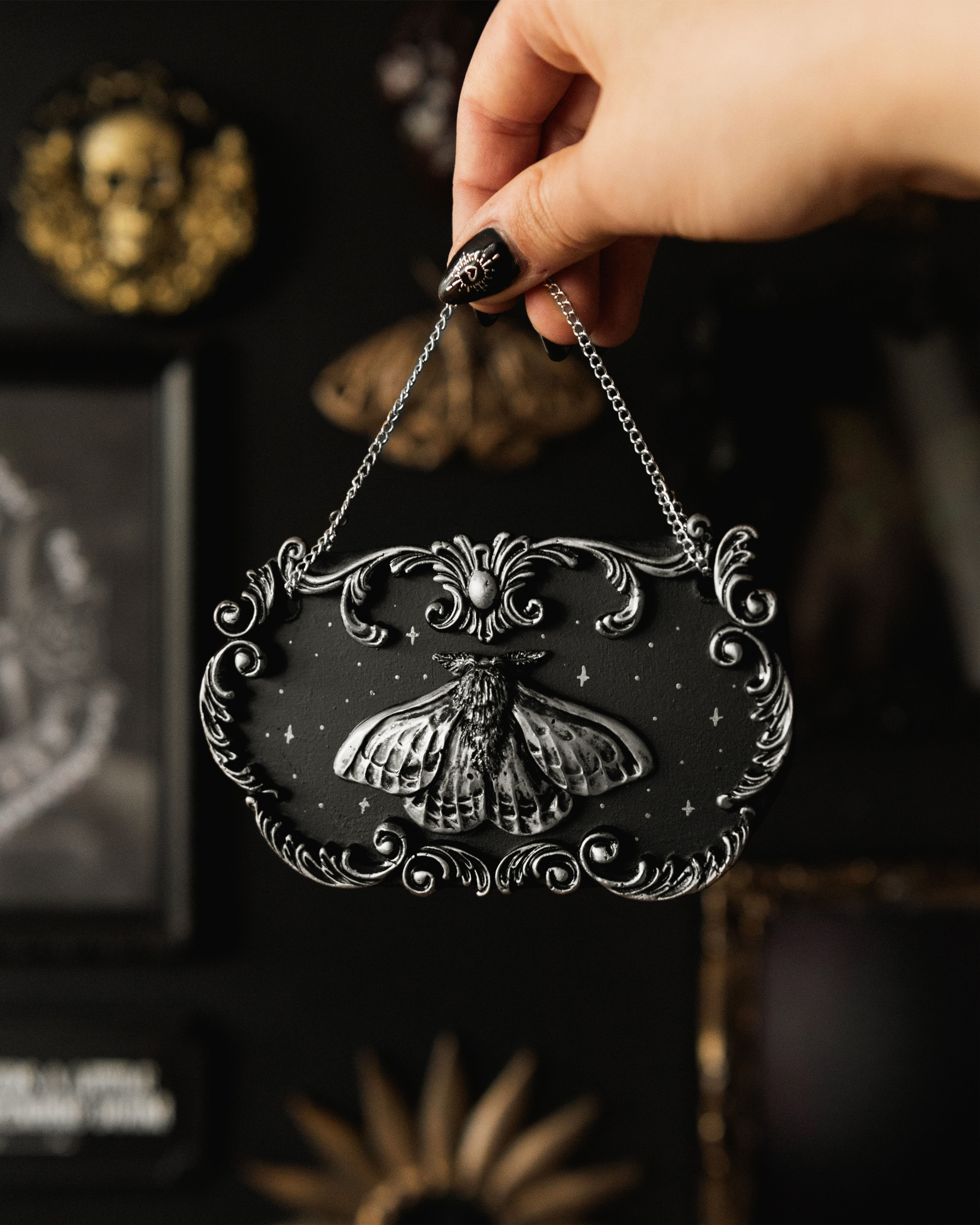 Ornate moth wall hanging with baroque frame, celestial black background and sculpted moth, hanging from a decorative chain.