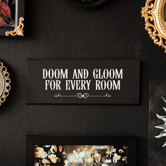 Black and white gothic style wall plaque with text saying 'Doom and gloom for every room' with a flourish beneath the text.