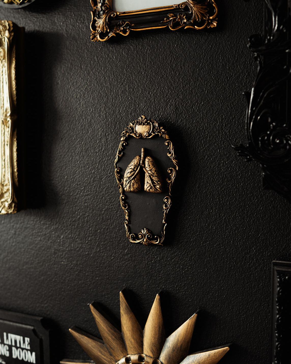 Coffin-shaped wall hanging with a baroque style edge and central hand-sculpted lungs. Available in black with silver or gold