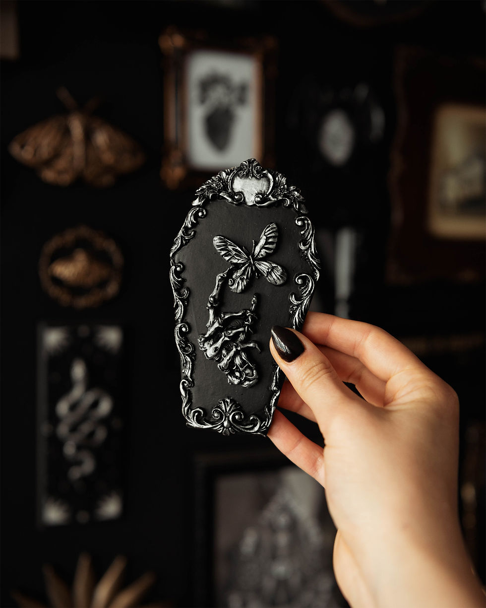 Thumbnail: Mini coffin shaped wall decor with a skeleton hand holding a butterfly in an ornate frame. Available in silver or gold.