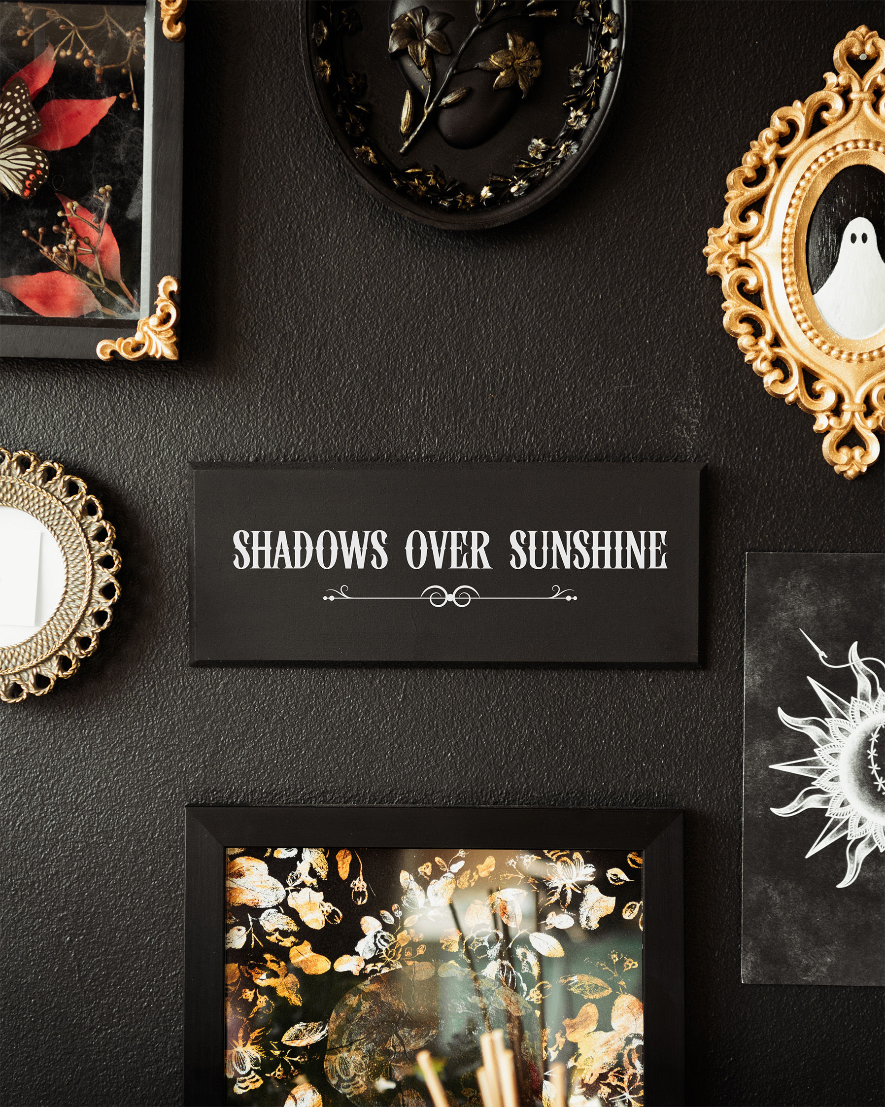 Black and white gothic style wall plaque with text saying ‘shadows over sunshine’ with a flourish beneath the text.