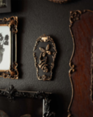 Mini coffin shaped wall decor with a skeleton hand holding a butterfly in an ornate frame. Available in silver or gold.