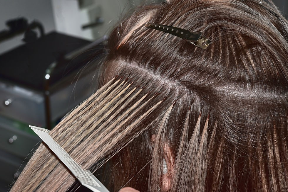 Hair extensions applied to blonde hair using fusion technique. Hands and tools are visible. Hair clips secure sections. Salon setting.
