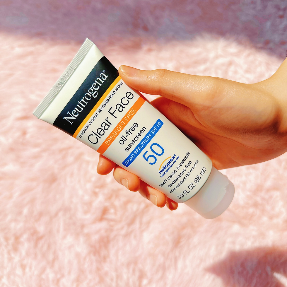 Hand holding a tube of Neutrogena Clear Face oil-free sunscreen SPF 50 against a pink fuzzy background, conveying a fresh, sunny mood.