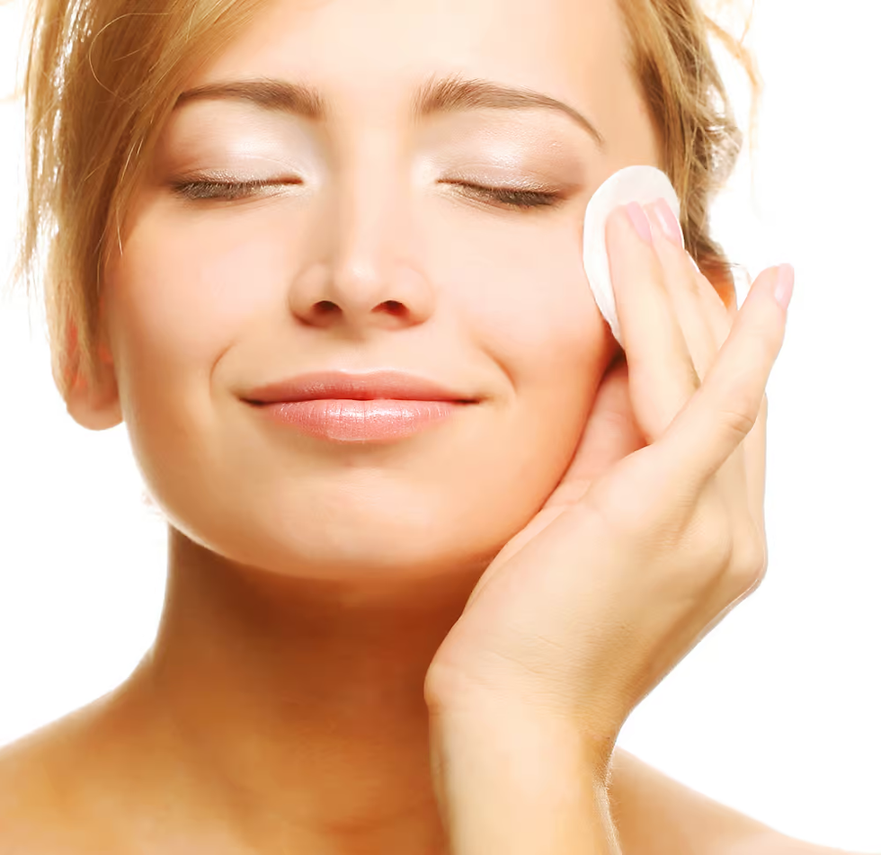 Woman with closed eyes, smiling, using a cotton pad on her cheek. Bright background, relaxed mood, light skin tones.
