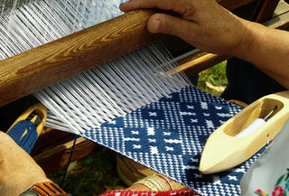 Artisan brodeuse en pleine démonstration dans un atelier textile du Jura, entourée de fils colorés et motifs traditionnels.
