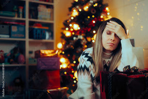 A woman sits with a weary expression next to a festive Christmas tree surrounded by wrapped gifts, capturing the overwhelming holiday stress amidst celebratory decorations.