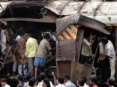 भीड़ एक दुर्घटना के बाद टूटे हुए दरवाज़ों से भरी एक क्षतिग्रस्त ट्रेन कार को बाहर निकालती है; हिंदी साइन पर लिखा है प्रथम श्रेणी।