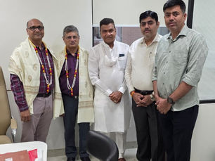 एक ऑफ़िस में पाँच आदमी पोज़ दे रहे हैं; उनमें से दो ने खास मौकों पर पहने जाने वाले शॉल ओढ़े हुए हैं और वे एक काले स्टूल व खिड़की के ब्लाइंड्स के पास खड़े हैं।