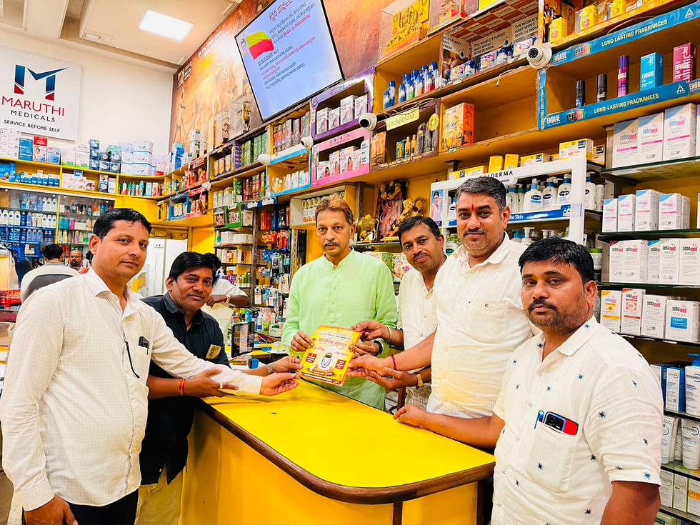 मारुति मेडिकल्स फ़ार्मेसी में छह आदमी काउंटर पर एक बुकलेट पकड़े हुए पोज़ दे रहे हैं; उनके आस-पास सामान से भरी शेल्फ़ और एक चमकदार टीवी डिस्प्ले है।
