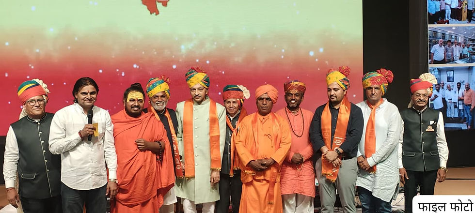 मंच पर पगड़ीधारी पुरुषों का समूह, बीच में माइक लिए वक्ता; पीछे लाल स्क्रीन और दाईं ओर फाइल फोटो