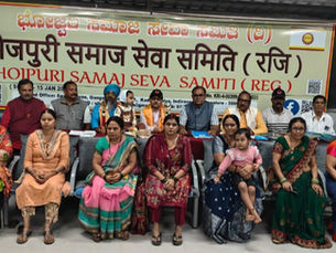 भोजपुरी समाज सेवा समिति की बैठक में मंच पर और सामने बैठे पुरुष–महिलाएँ, पीछे बड़ा बैनर, औपचारिक माहौल