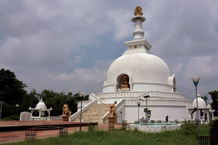 White temple under cloudy sky, featuring steps and lion statues. Green grass in foreground, serene and peaceful setting.