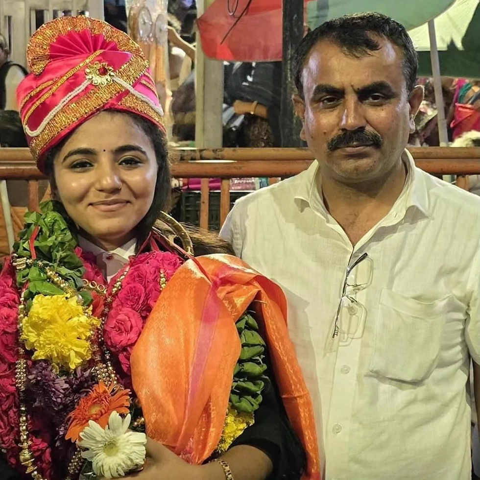 रंग-बिरंगे पारंपरिक परिधान और फूलों की मालाओं में मुस्कुराती युवती, सफेद शर्ट वाला पुरुष साथ, भीतर का दृश्य