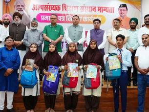 अधिकारी और छात्र एक हिंदी कार्यक्रम में पोज़ दे रहे हैं; लड़कियां किताबें और बैकपैक पकड़े हुए हैं; पीछे बैनर लगा है और माहौल जश्न वाला है।