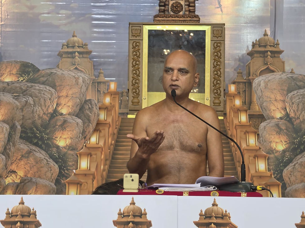 Shirtless monk speaks at a podium with a microphone, gesturing before a temple-themed backdrop and papers.