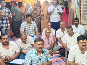 Indoor group of men and veiled women clapping in a decorated room with orange walls, sitting on mats in a lively gathering.