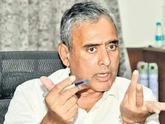 एक कार्यालय में सफेद शर्ट पहने अधेड़ उम्र का व्यक्ति कुर्सी पर बैठकर हाथ में कलम लेकर इशारा करते हुए गंभीरता से बोलता है।