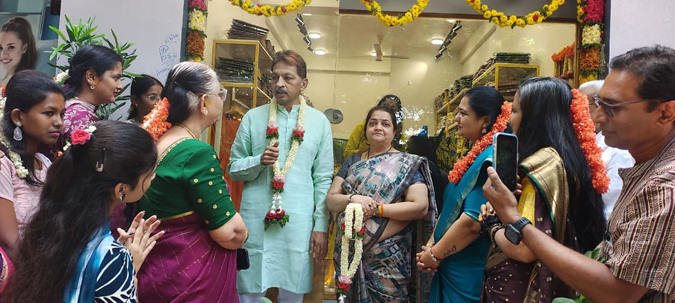 फूलों से सजे दुकान के दरवाज़े पर फूलों की माला पहने लोगों का एक समूह इकट्ठा है; हल्के हरे रंग के कपड़े पहने एक व्यक्ति बात कर रहा है, महिलाएँ सुन रही हैं और एक महिला फ़ोन पर रिकॉर्डिंग कर रही है।
