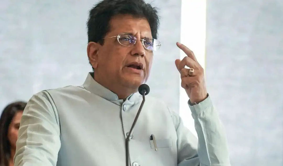मंच पर माइक के सामने चश्मा पहने व्यक्ति बोलते हुए, उंगली उठाए; हल्की पृष्ठभूमि में गंभीर माहौल।
