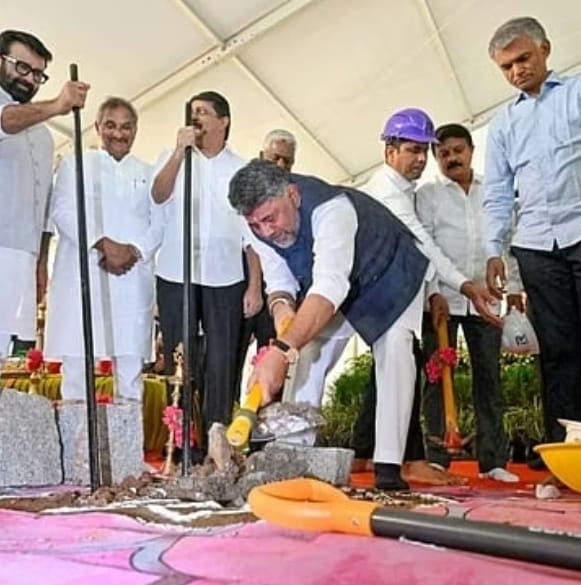 एक सफ़ेद टेंट के नीचे आयोजित समारोह में कुछ पुरुष मौजूद हैं; उनमें से एक पीले रंग के औज़ार से ज़मीन खोद रहा है जबकि बाकी लोग उसे देख रहे हैं; वहाँ गुलाबी फ़र्श और फावड़े भी हैं।