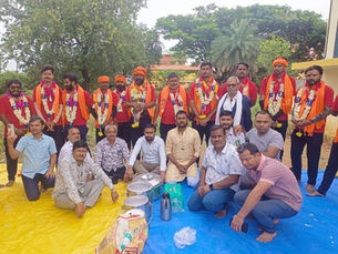 Group of men posing outdoors on tarps, many in red shirts and garlands, with cooking pots; Hindi text फाइल फोटो.