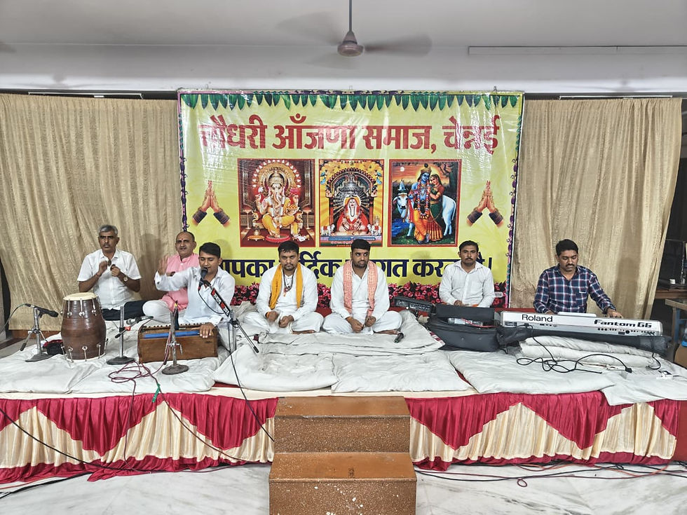 मंच पर भक्ति संगीत मंडली, गायक व वादक; पीछे गणेश-शिव-राधा-कृष्ण चित्रों वाला बैनर, वातावरण आध्यात्मिक