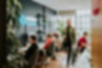 A modern office with four people working at desks. One person is standing and blurred in motion.