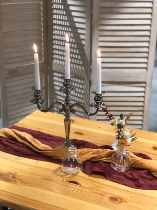 Table avec dessus un chemin de table en tissu et un bougeoir avec trois bougies