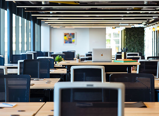 Modern office interior featuring communal work tables, structured seating, and linear ceiling lighting.