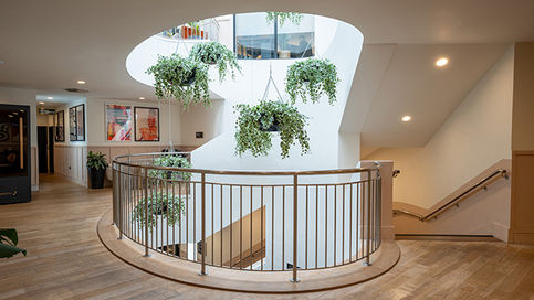Interior atrium with staircase and circular balcony with hanging plants.