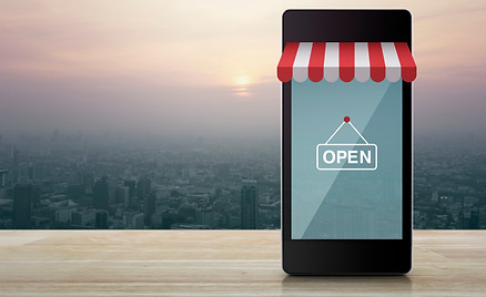 Modern smart mobile phone with on line shopping store graphic and open sign on wooden tabl