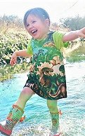 Little girl splashing in water wearing a dress in fun dinosaur print. Dress is handmade in 100% woven cotton fabric and is fully lined. By Lavish Lilac