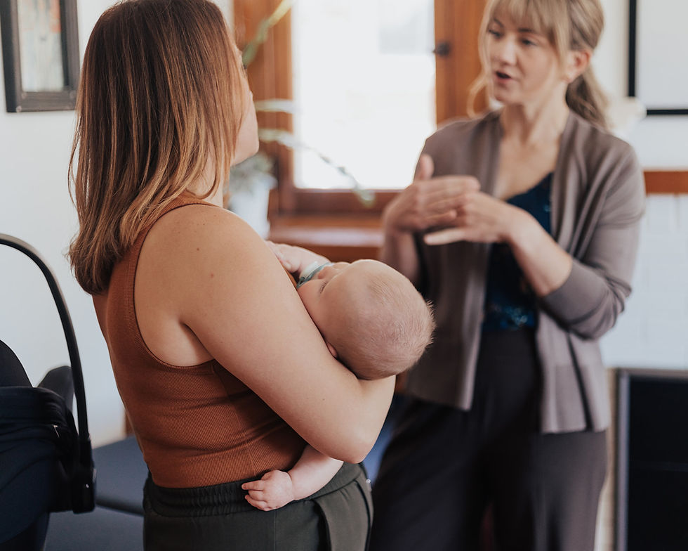 Woman holding a baby while talking with a physical therapist in a bright room.